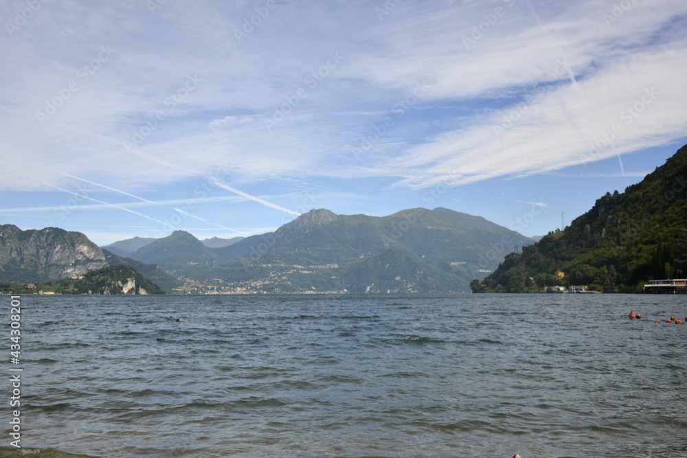 Horizontal panorama of mountain lake surrounded by hills covered with green cedar forest. Italy Lierna, June 22 2018.