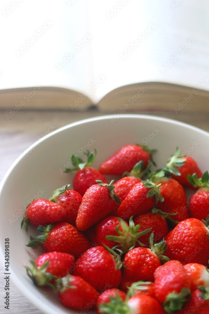 Bowl of strawberries and open book on a table. Selective focus.