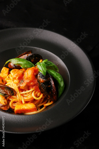 pasta with seafood closeup with black plate on dark background. Italian spaghetti pasta with Mussels, shrimp and tomatoes
