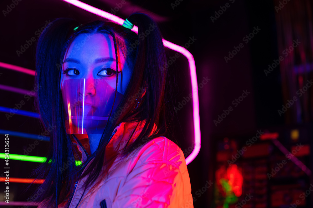 young asian woman in face shield near neon lighting young asian woman in face shield near neon lighting