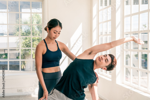 Diversity group of people do yoga workout together. Asian female instructor check male student pose.