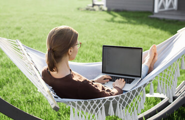 Woman using laptop outdoor. Young beautiful girl in a hammock and working on computer. Freelance, summer, enjoy life, student lifestyle, distance studying, travel vacations, online learning concept