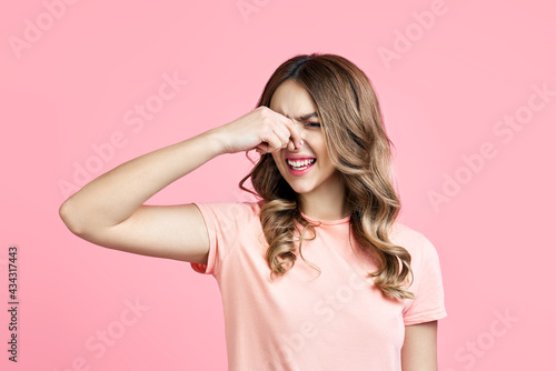 Smells bad, woman pinching nose with disgust on pink background