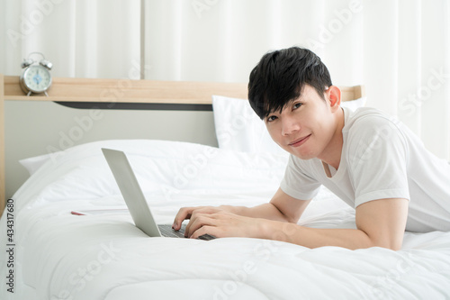 young man playing internet on laptop in bedroom.