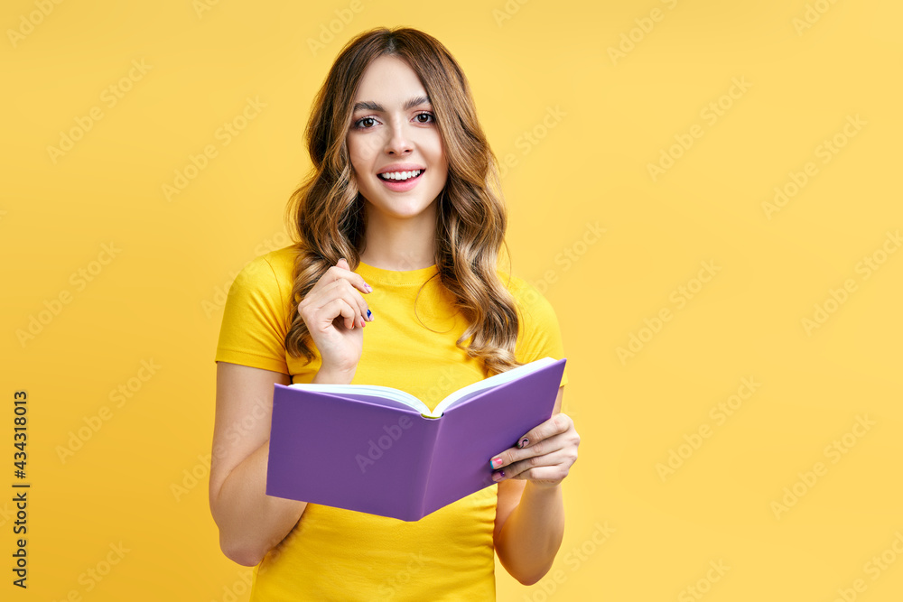 Smiling positive girl reading book on yellow background Smiling positive girl reading book on yellow background