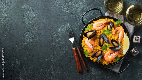 Traditional spanish seafood paella in pan with chickpeas, shrimps, mussels, squid on black concrete background. Top view with copy space. Banner