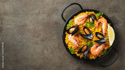 Quadro su tela Traditional spanish seafood paella in pan with chickpeas, shrimps, mussels, squid on brown concrete background