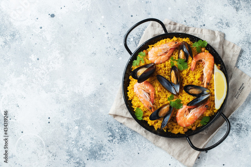 Traditional spanish seafood paella in pan with chickpeas, shrimps, mussels, squid on light grey concrete background. Top view with copy space photo