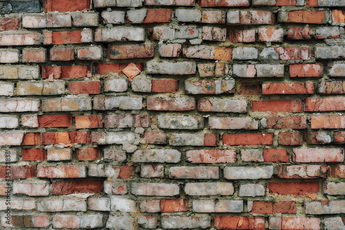 Old and broken brick  a sample of a brick wall in various shades of red  gray  orange and beige  sometimes covered with greenish mold. Wall texture and background for vintage wallpaper. 