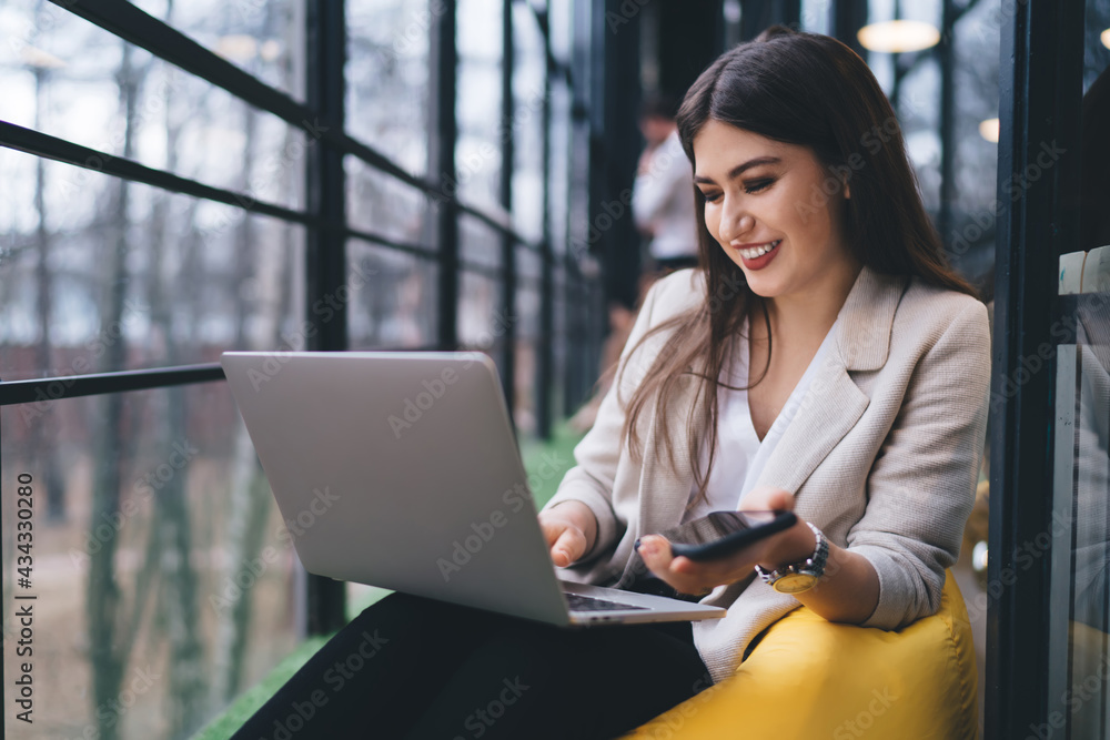 Positive woman with smartphone working on laptop Positive woman with smartphone working on laptop