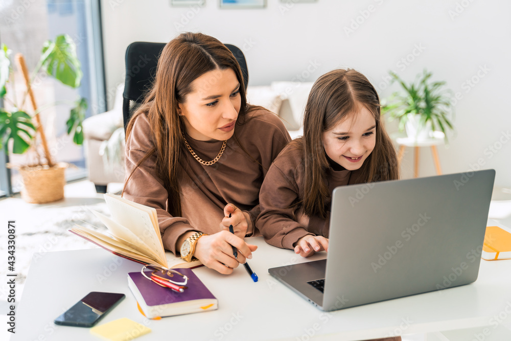Mom and little daughter doing homework on laptop. Mother teaches the child at home Mom and little daughter doing homework on laptop. Mother teaches the child at home