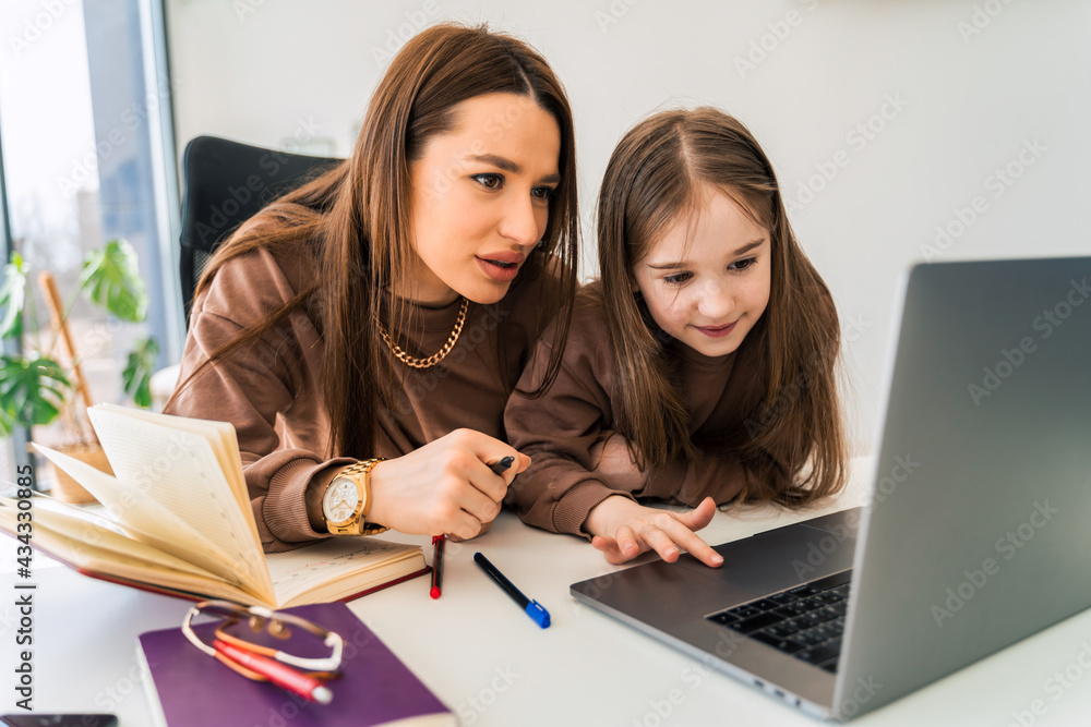 Mom and little daughter doing homework on laptop. Mother teaches the child at home Mom and little daughter doing homework on laptop. Mother teaches the child at home