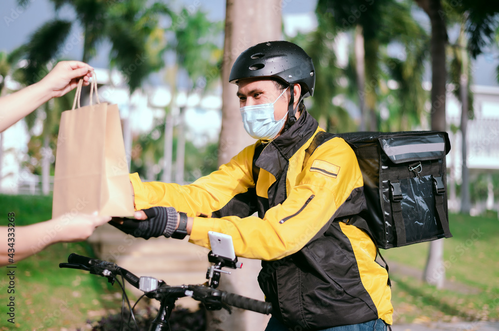 Courier wearing a yellow company shirt, riding a bicycle, delivering food paper bags to customers Courier wearing a yellow company shirt, riding a bicycle, delivering food paper bags to customers