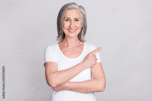 Photo of shiny pretty age woman dressed white outfit smiling pointing finger empty space isolated grey color background