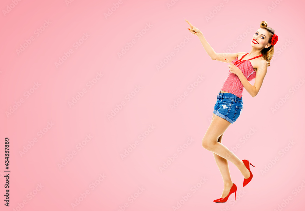Full body portrait - amazed happy woman pointing at something. Excited girl in pin up style, showing copy space for text or imaginary. Retro fashion and vintage. Rose pink color background.