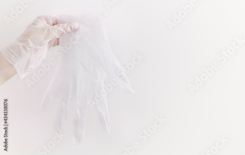 One female hand holding transparent vinyl glove ready for recycle above neutral background with copy space