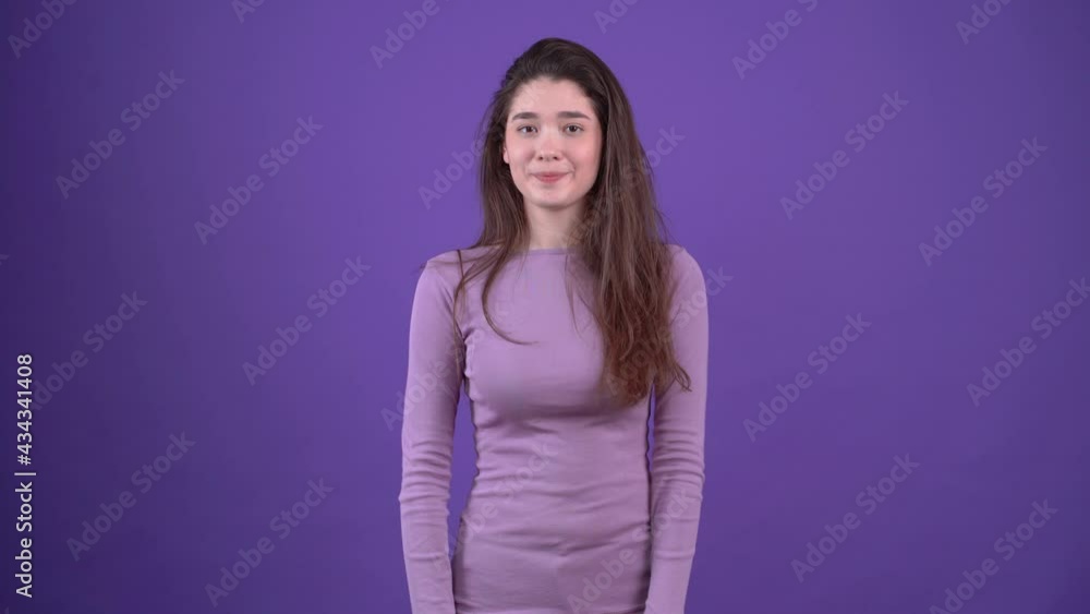 The charismatic young woman looks conspiratorial and shows with her hand the like sign displaying a mysterious smile. Brunette isolated on a purple background, dressed in a purple sweater. Lifestyle The charismatic young woman looks conspiratorial and shows with her hand the like sign displaying a mysterious smile. Brunette isolated on a purple background, dressed in a purple sweater. Lifestyle