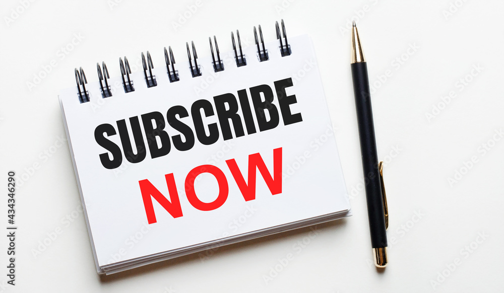 On a light background, a white notebook with are words SUBSCRIBE NOW and a pen. On a light background, a white notebook with are words SUBSCRIBE NOW and a pen.