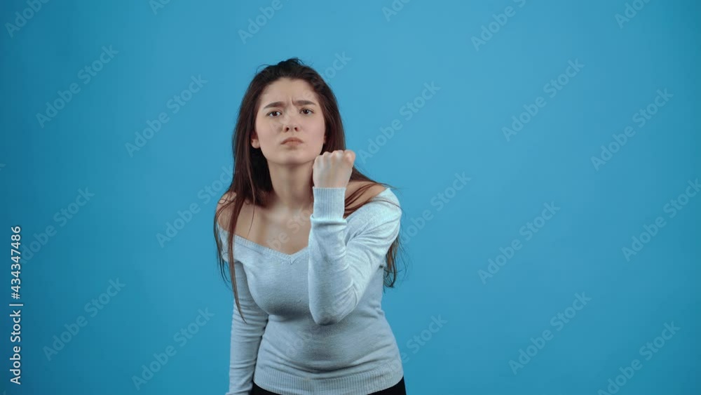 The angry young woman points her finger at her nose, you are not ashamed, then she points with her fist, you will be beaten. Asian with dark hair, dressed in a blue blouse, isolated on a dark blue The angry young woman points her finger at her nose, you are not ashamed, then she points with her fist, you will be beaten. Asian with dark hair, dressed in a blue blouse, isolated on a dark blue