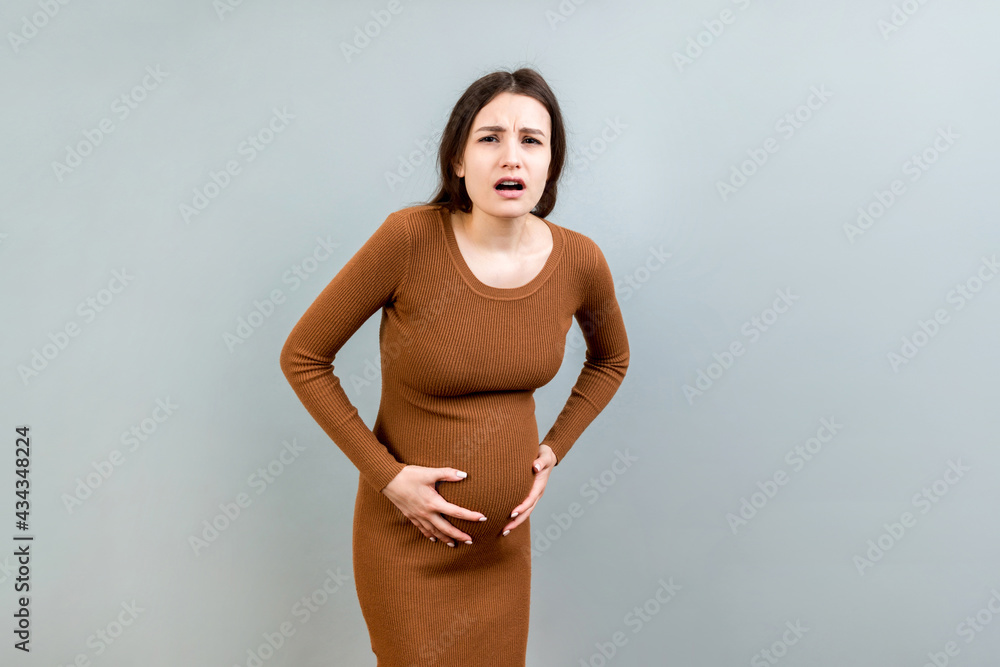 a pregnant girl who has a stomach ache stands on a colored background. isolated a pregnant girl who has a stomach ache stands on a colored background. isolated