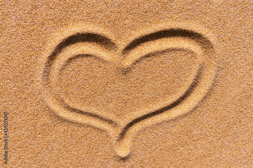 The symbol of the heart drawn on a sand. Background close up of a golden sunny sandy beach.