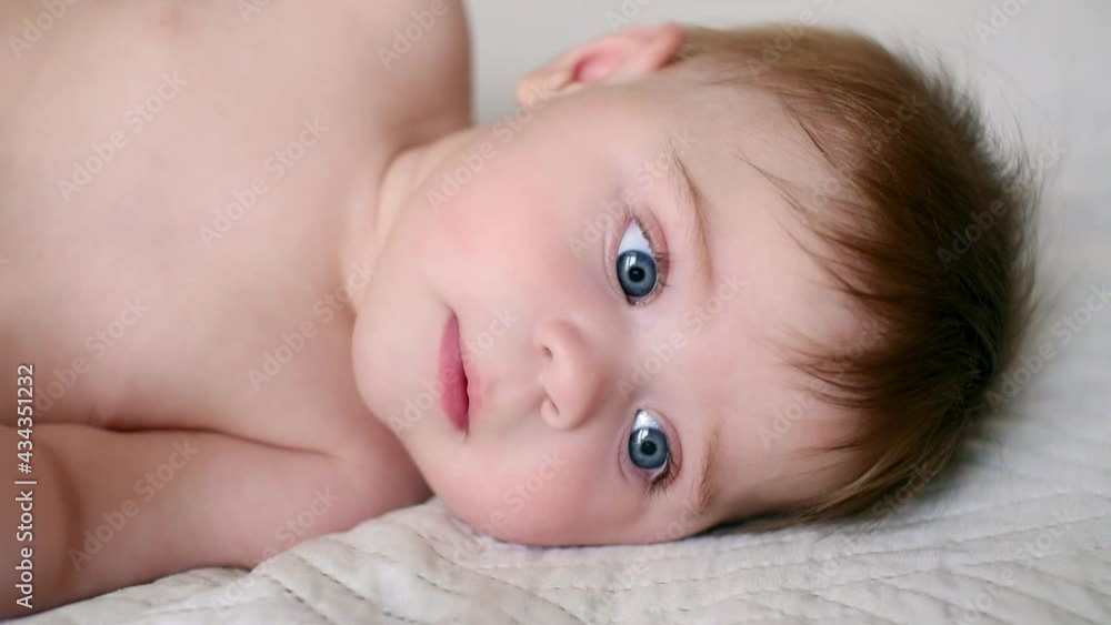 Naked baby lying on bed smiles and plays. Cute infant lying on the back. Close up of baby face looking for something interesting. Naked baby lying on bed smiles and plays. Cute infant lying on the back. Close up of baby face looking for something interesting.