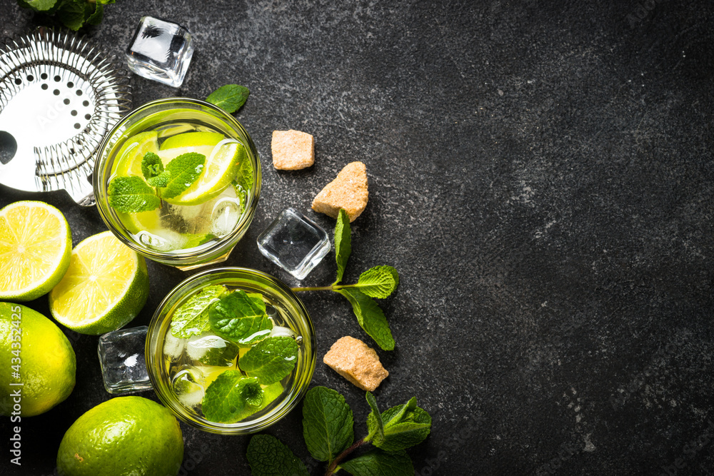 Mojito cocktail with ingredients on black stone background. Summer drink mojito with lime, rum, mint and ice. Top view copy space.