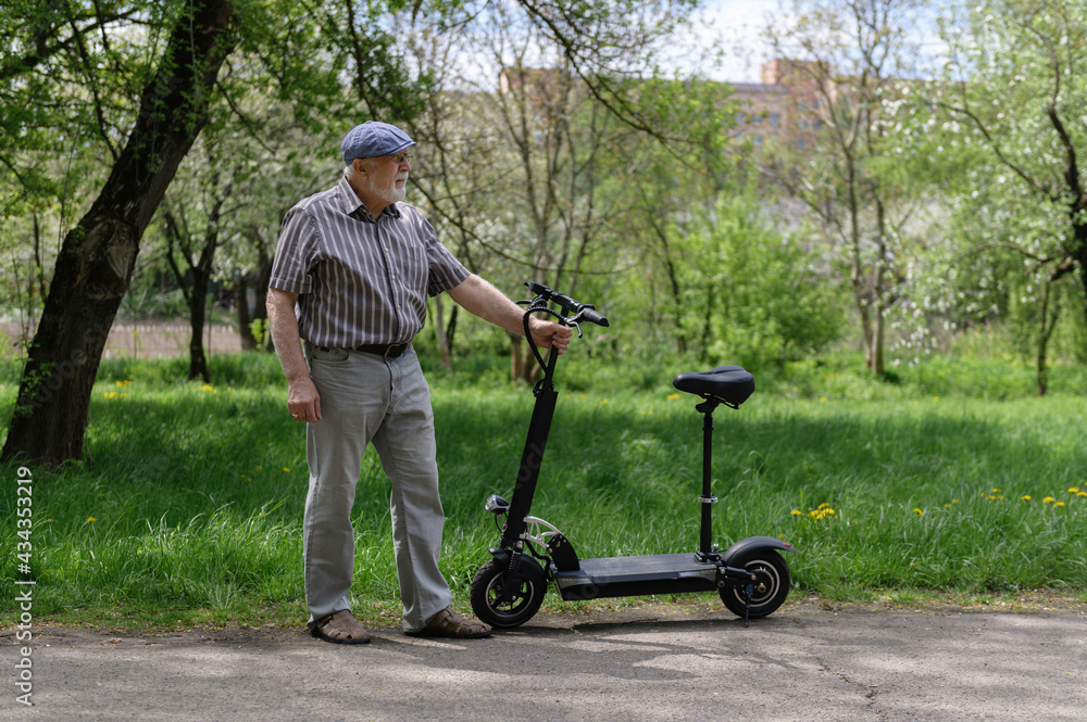 A positive, elderly man went for a walk to the park, stopped and was holding an eco scooter behind the wheel. Healthy lifestyle of the elderly.