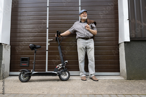 A positive, elderly man stands near the door and holds an eco scooter behind the wheel. Healthy lifestyle of the elderly. photo