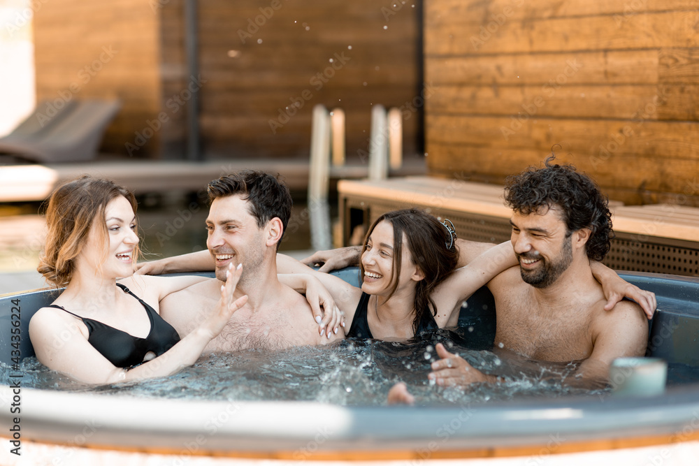 Company of friends steaming in a vat outdoors near the spa and lake. Women and man have fun and relax in wellness center. 