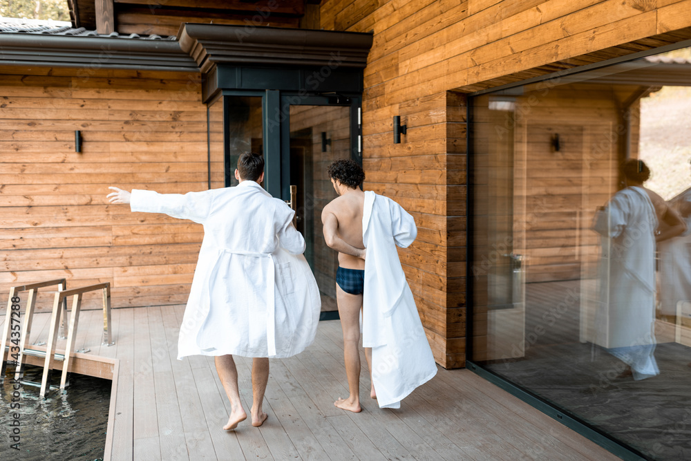 Company of male friends walking on the terrace in spa complex while dressing on the go their bathrobe. Relax and fun time in wellness spa. 
