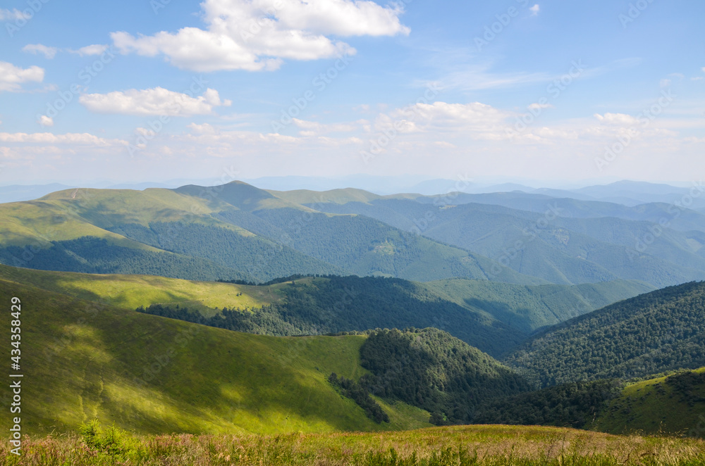 White summer clouds overt the mountains covered green forest and grassy slopes Borzhava mountain range, popular travel destination of Ukraine. Carpathian Mountains