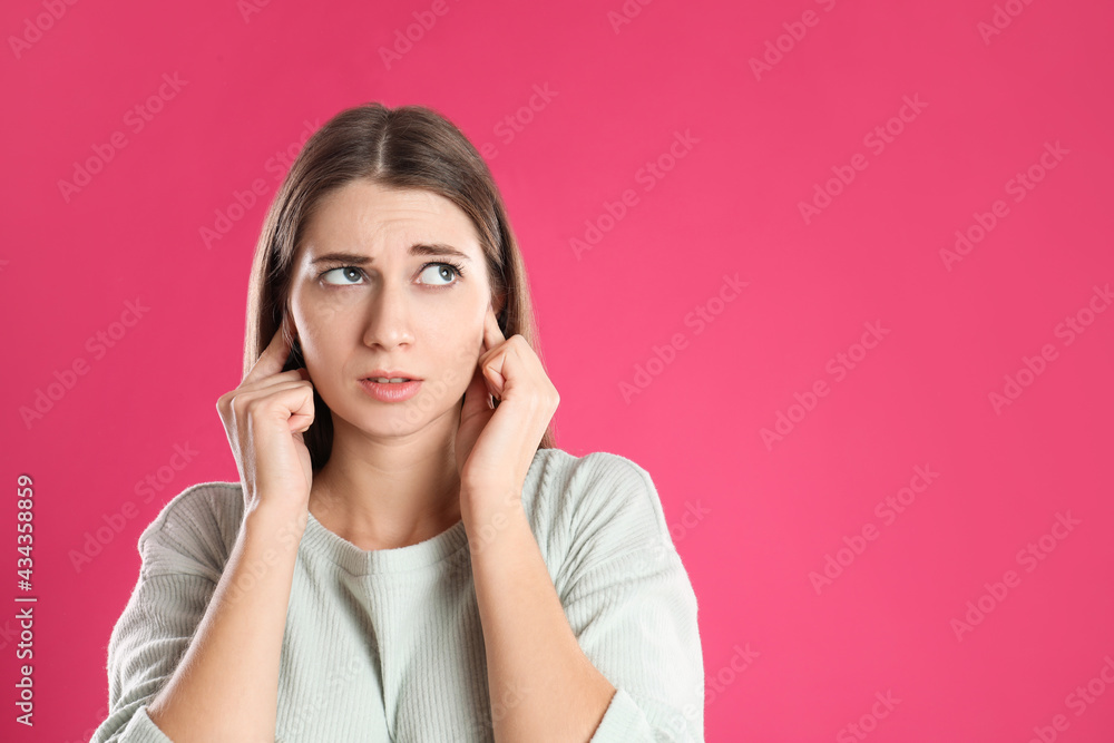 Emotional young woman covering her ears with fingers on pink background. Space for text Emotional young woman covering her ears with fingers on pink background. Space for text