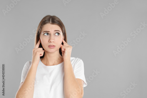 Emotional young woman covering her ears with fingers on grey background. Space for text