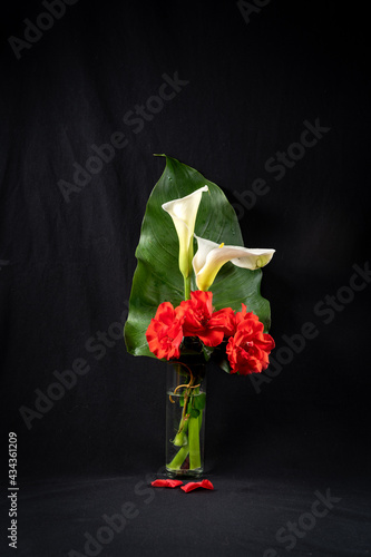 Beautiful bouquet of flowers and leaves of arum and red roses, on a black background photo