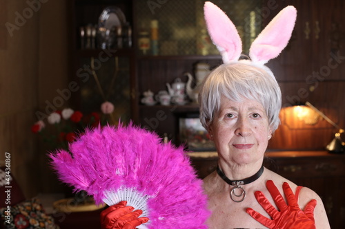 Fun senior woman with bunny ears and feathers hand fan photo
