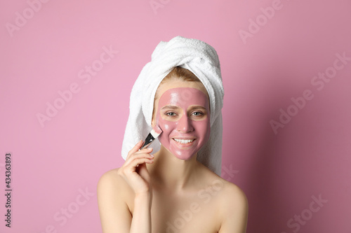 Young woman applying pomegranate face mask on pink background