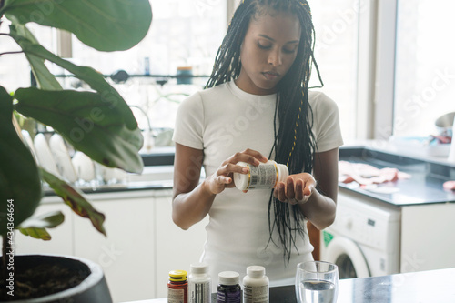 African American woman taking vitamins and supplements at home in her kitchen