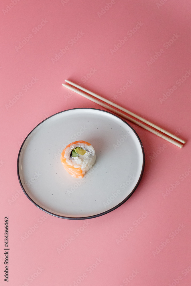 sushi roll Philadelphia on a plate on a pink background. Delicious fresh roll with curd cheese, avocado and salmon sushi roll Philadelphia on a plate on a pink background. Delicious fresh roll with curd cheese, avocado and salmon