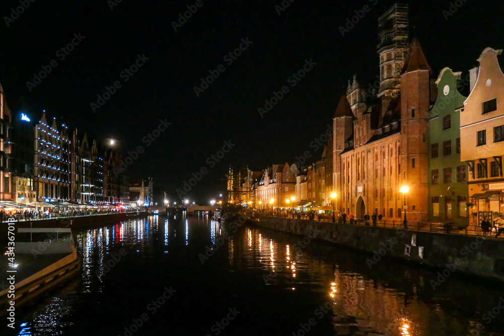 A night view on the shores of Martwa Wisla flowing through Gdansk in Poland, with medieval port crane. New architecture meeting with medieval constructions. The city lights reflecting in the river.