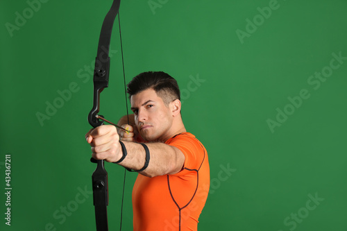 Man with bow and arrow practicing archery on green background, space for text