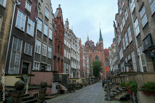 A deserted street in Old Town of Gdansk, Poland. The both sides of a paved alley have tall medieval buildings with colorful facades. Bell tower at the end of the alley. A bit of overcast. City tour. © Chris