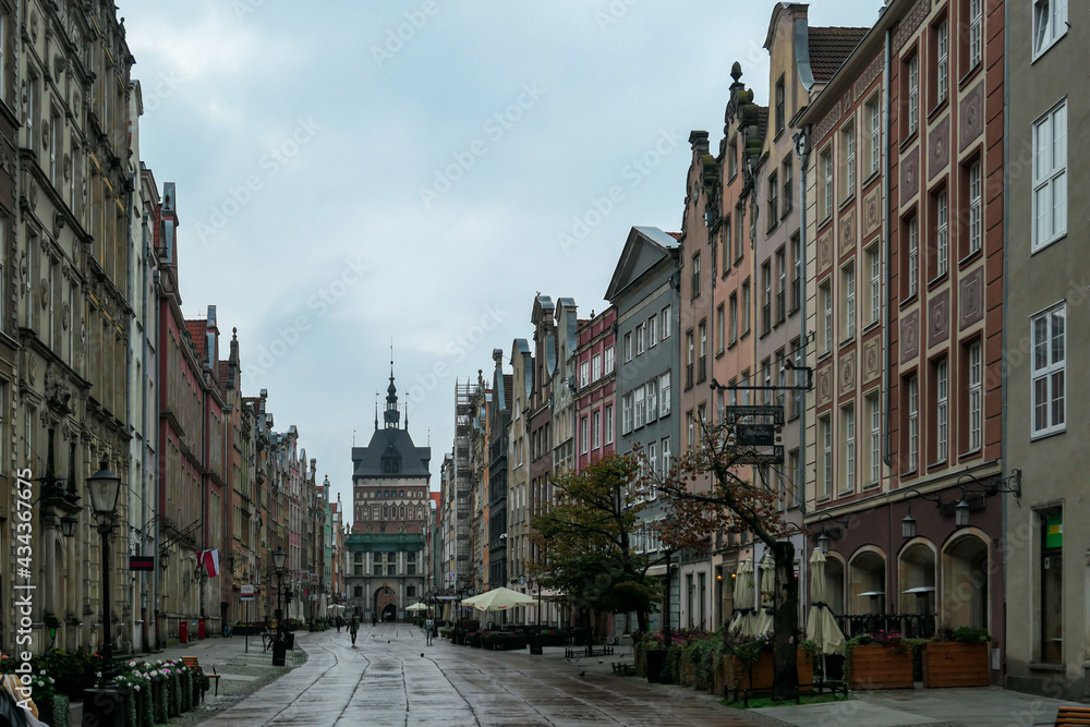 A deserted street in Old Town of Gdansk, Poland. The both sides of a paved alley have tall medieval buildings with colorful facades. Bell tower at the end of the alley. A bit of overcast. City tour.