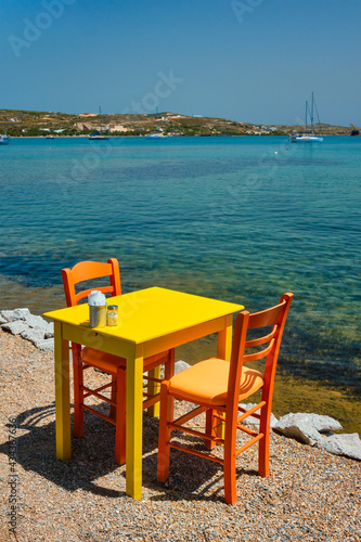 Cafe tableon beach in Adamantas town on Milos island with Aegean sea with boats in background