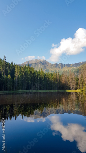 A panoramic view on Smreczynski Staw in Tatra Mountains in Poland. Glacial tarn at the mouth of Pysznianska Valley. The high Tatra chains are reflecting in the calm surface of the lake. White clouds