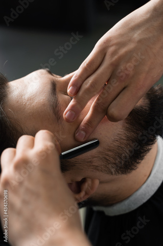 Straight razor cut mans beard in barbershop. Barber man making hairstyle for handsome man.
