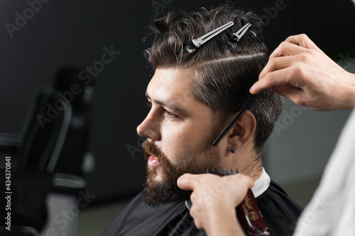 Barber making hairstyle for confident bearded hipster. Advertising for barbershop and men's beauty salon.