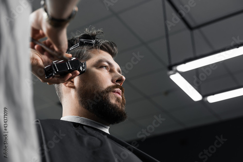 Low fade machine haircut for handsome bearded man in barbershop. Barber with dread locks making hairstyle with a smooth transition.