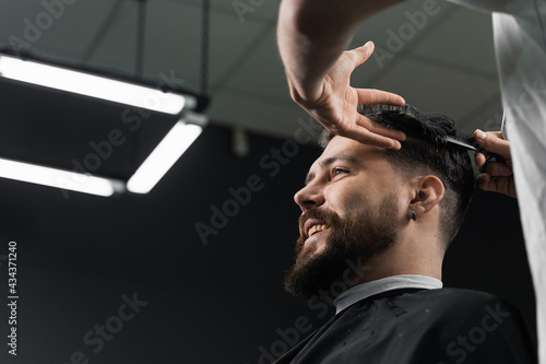 Low fade machine haircut for handsome bearded man in barbershop. Barber with dread locks making hairstyle with a smooth transition.