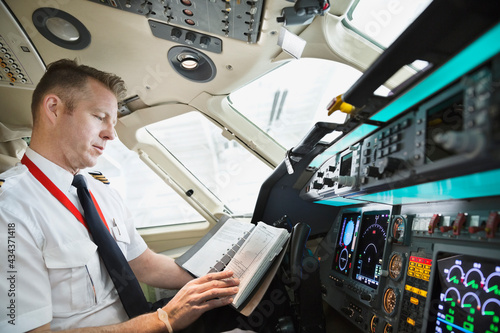 Photo Male pilot checking logbook in airplane cockpit